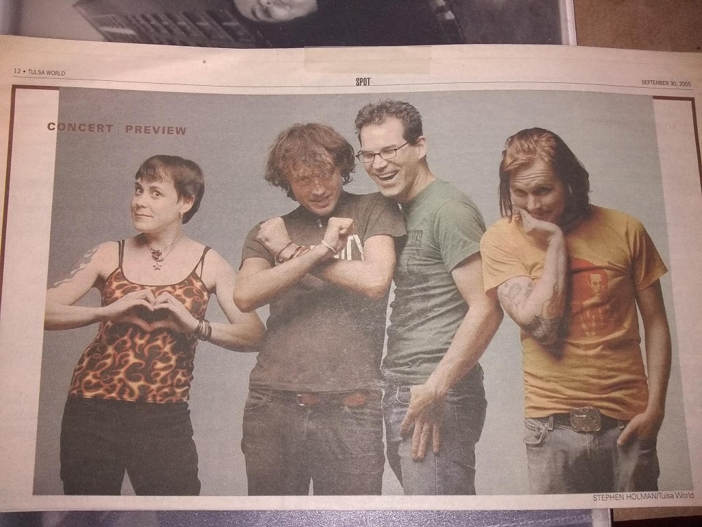A picture of four people in a newspaper, arranged side by side. Each looks like a musician. The one on the right has very dumb, shoulder-length reddish hair. It looks greasy.